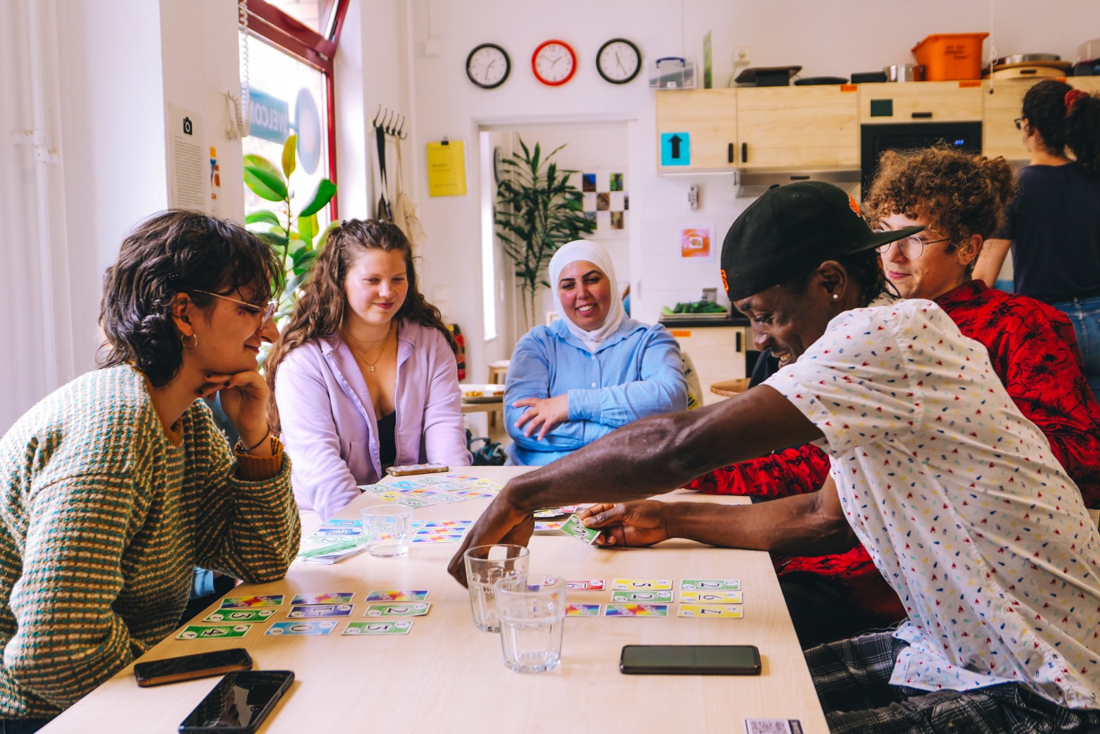 vier Menschen sitzen an einem Tisch und spielen ein Kartenspiel